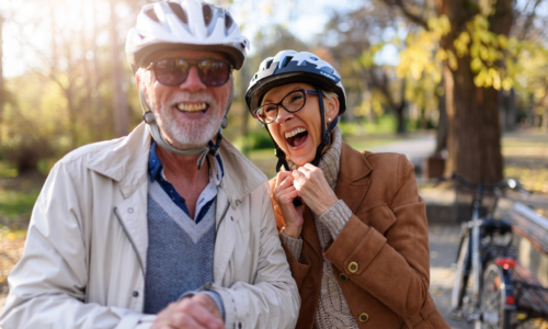 Cheerful active senior couple with bicycle in public park togeth