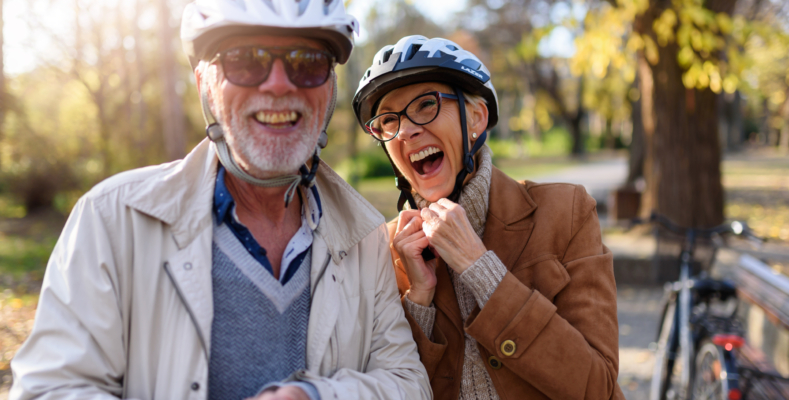 Cheerful active senior couple with bicycle in public park togeth