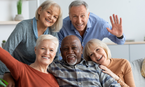 Multiracial group of happy positive elderly people men and women in casual outfits taking selfie together while chilling together, hugging and smiling at camera, nursing home interior