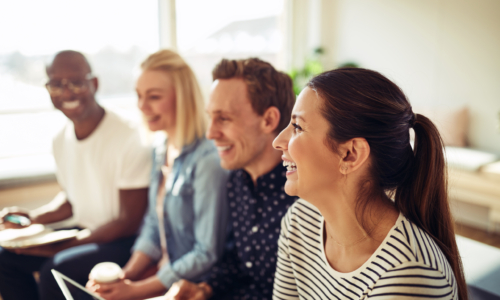 Diverse group of businesspeople laughing while sitting in a row together during a presentation in an office