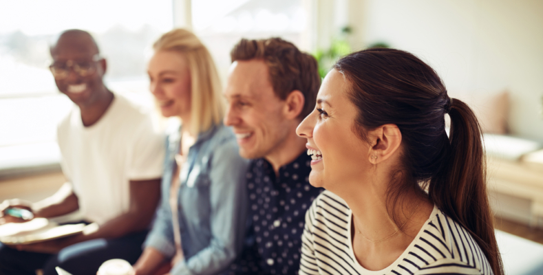 Diverse group of businesspeople laughing while sitting in a row together during a presentation in an office